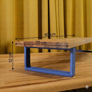 May include: A wooden shelf with a blue metal frame. The shelf measures 80 cm long, 20 cm wide, and 12 cm high. The wood has a natural grain, and the frame is a solid blue colour. The shelf is designed for display or storage.
