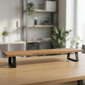 Puede incluir: Un soporte de monitor de madera con una parte superior rectangular y patas de metal negro. El soporte está hecho de madera de color marrón claro y tiene un diseño minimalista. El soporte mide aproximadamente 76 cm de largo.