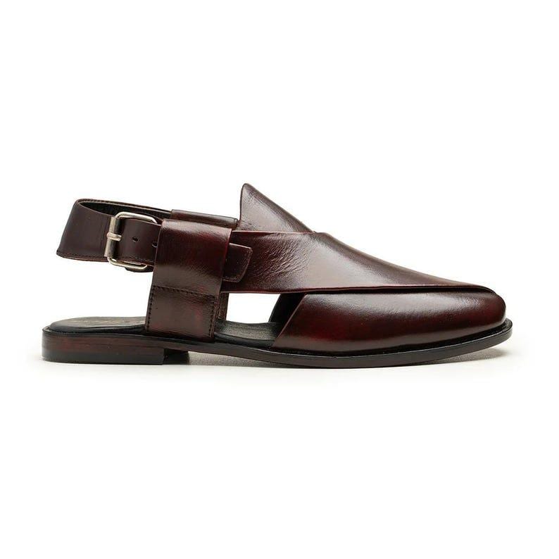 May include: A single, dark burgundy leather sandal. The sandal has a distinctive design with a strap and silver buckle. It features a pointed toe and cut-out detailing. The sole is black. The sandal is set against a white background.