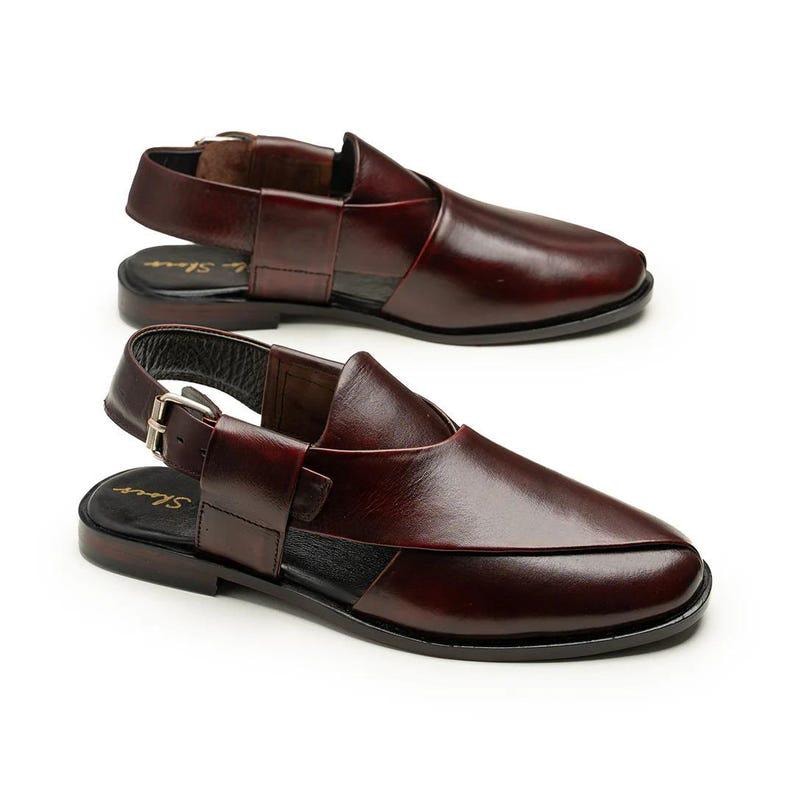 May include: Two pairs of burgundy leather sandals with a slingback design. The sandals have a buckle closure and a closed-toe design. The soles are black, and the sandals are displayed on a white background. The sandals are a type of footwear.
