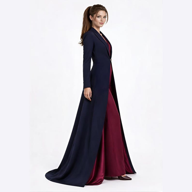 May include: A floor-length navy blue coat with long sleeves and a single button closure at the waist, worn over a solid deep burgundy sleeveless gown. The coat features a structured lapel collar and a full-length skirt that trails slightly behind.