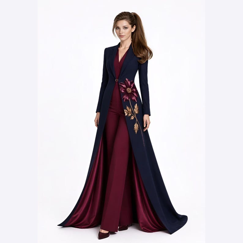May include: A floor-length navy blue coat with a single button closure and a large floral embroidery in shades of burgundy and gold on the front, worn over a solid burgundy jumpsuit with wide-leg trousers and a V-neckline.