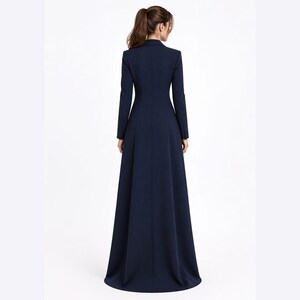 May include: A floor-length navy blue coat dress featuring a structured collar, long sleeves, and a fitted bodice that transitions into a flared, full-length skirt. The garment is shown from the back, displaying a clean, solid-coloured design.