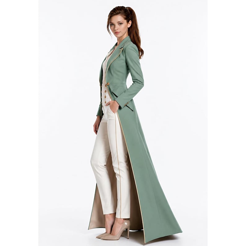 May include: A sage green floor-length coat with a tailored fit, long sleeves, and a notched lapel. The coat features a single-breasted front with gold-toned buttons and a contrasting beige lining. It is worn over a white top and white trousers.