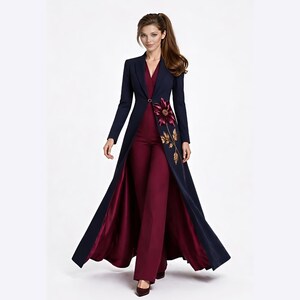 May include: A long-sleeved navy blue coat with a single button closure, worn over a deep burgundy jumpsuit. The coat features a large embroidered floral design in shades of burgundy and gold on the left side, with a satin-finish burgundy lining.