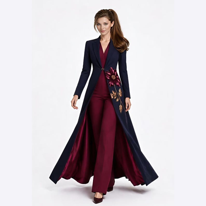 May include: A long-sleeved navy blue coat with a single button closure, worn over a deep burgundy jumpsuit. The coat features a large embroidered floral design in shades of burgundy and gold on the left side, with a satin-finish burgundy lining.