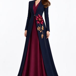 May include: A floor-length gown featuring a deep burgundy sleeveless dress paired with a long-sleeved navy blue coat. The coat has a single button closure at the waist and is decorated with a large embroidered burgundy flower and gold leaves.