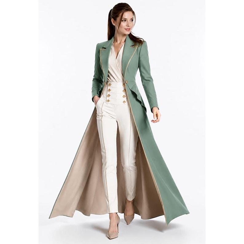 May include: A sage green floor-length coat with long sleeves, a single button closure, and gold piping trim, worn over a cream-colored wrap blouse and high-waisted cream trousers featuring two vertical rows of gold buttons and side pockets.