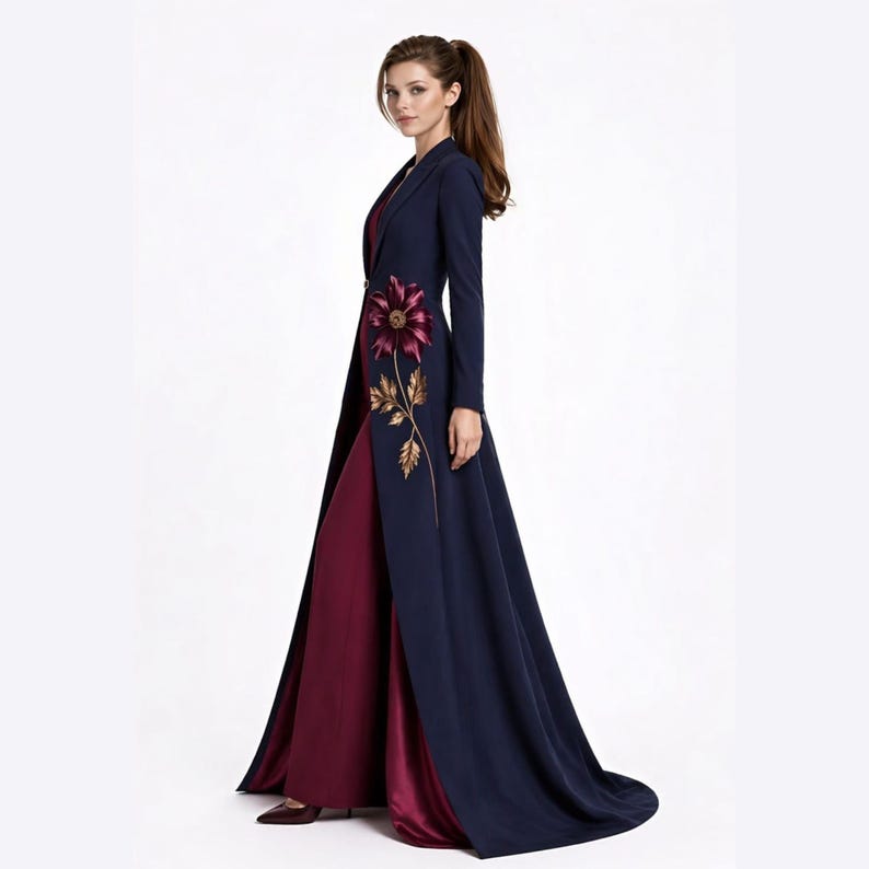 May include: A floor-length navy blue coat with long sleeves and a single button closure, featuring an embroidered burgundy flower with gold leaves on the front. The coat is worn over a solid burgundy floor-length dress with a smooth finish.