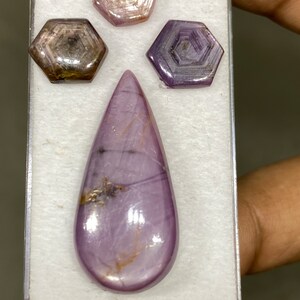 Könnte beinhalten: Drei violette sternförmige Edelsteine und ein tropfenförmiger violetter Edelstein mit goldenen Einschlüssen, alle auf weißem Hintergrund präsentiert.