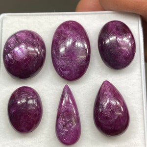 May include: Six purple gemstones of various shapes and sizes, including oval, pear, and round, displayed in a white box.