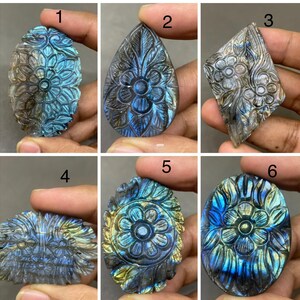 May include: A collection of six carved labradorite gemstones. Each gemstone features intricate floral designs, with variations in shape including oval, teardrop, and diamond. The stones display iridescent blue, green, and gold hues.