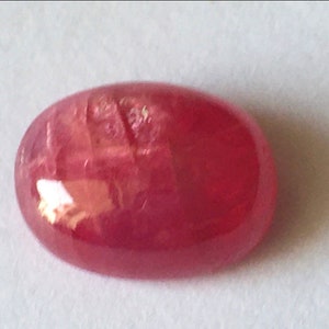 May include: A pink oval-shaped gemstone with a smooth, polished surface.