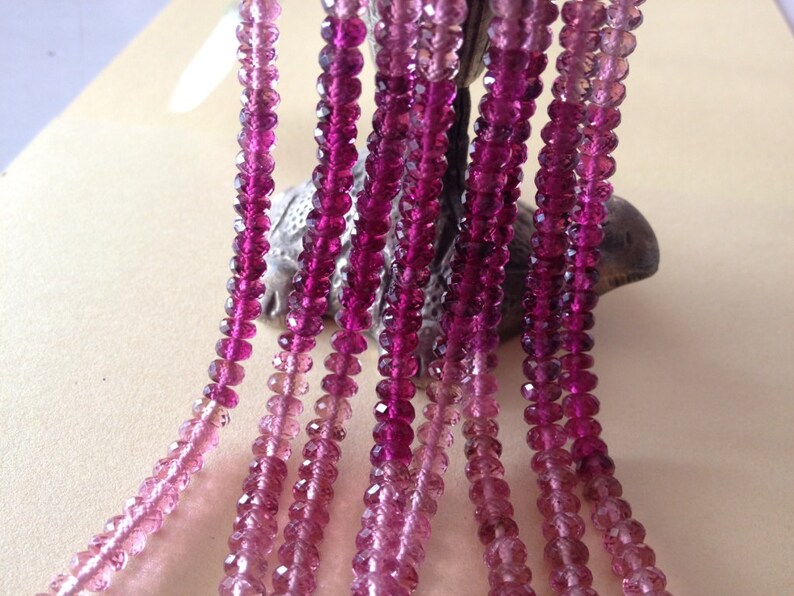 May include: Multiple strands of faceted pink and magenta gemstones. The beads are strung together, creating a gradient effect from light pink to deep magenta. The gemstones are displayed against a neutral background.
