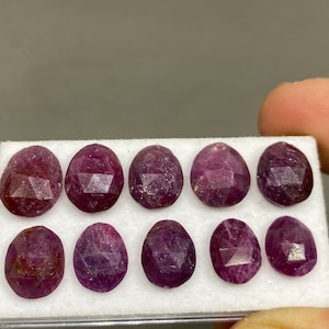 Puede incluir: Nueve gemas de rubí facetadas en una bandeja de espuma blanca. Los rubíes son de color rojo intenso y tienen un acabado pulido.