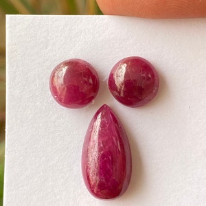 Puede incluir: Tres piedras preciosas de rubí, dos redondas y una en forma de pera, sobre un fondo blanco.