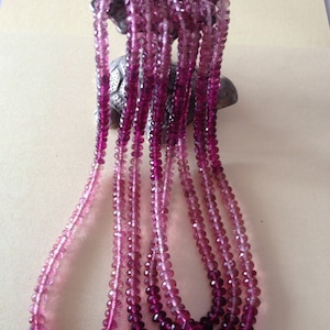 May include: Multiple strands of pink and purple faceted beads. The beads are strung together, resembling necklaces. The colour gradient ranges from light pink to deep purple. The beads are likely made of a translucent material, catching the light.