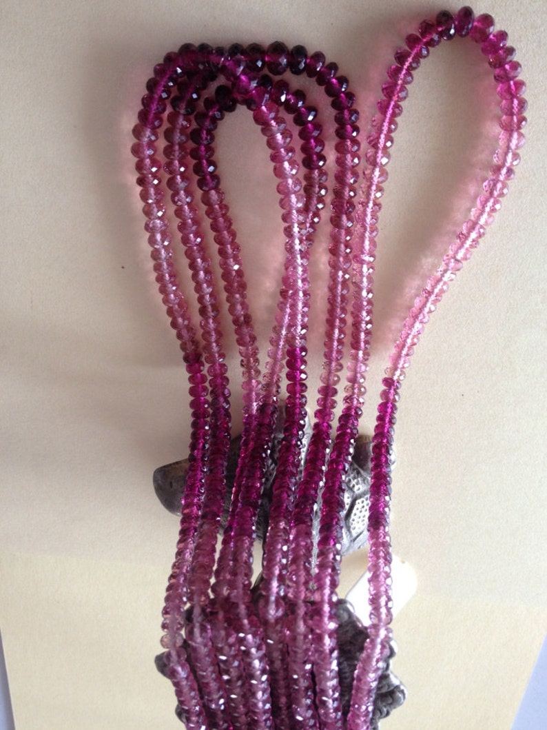 May include: A collection of pink and purple beaded necklaces. The beads are round and faceted, with a colour gradient from deep purple to pale pink. The necklaces are displayed against a neutral background.