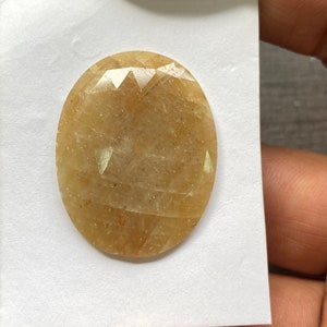 Pode incluir: Uma gema ovalada de cor castanho claro com um corte facetado. A gema tem uma aparência translúcida com um ligeiro tom amarelo.