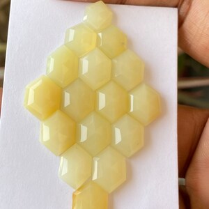 Peut inclure: Une collection de 15 pierres pr&eacute;cieuses hexagonales en cabochon jaune p&acirc;le dispos&eacute;es en nid d'abeille sur une carte blanche.