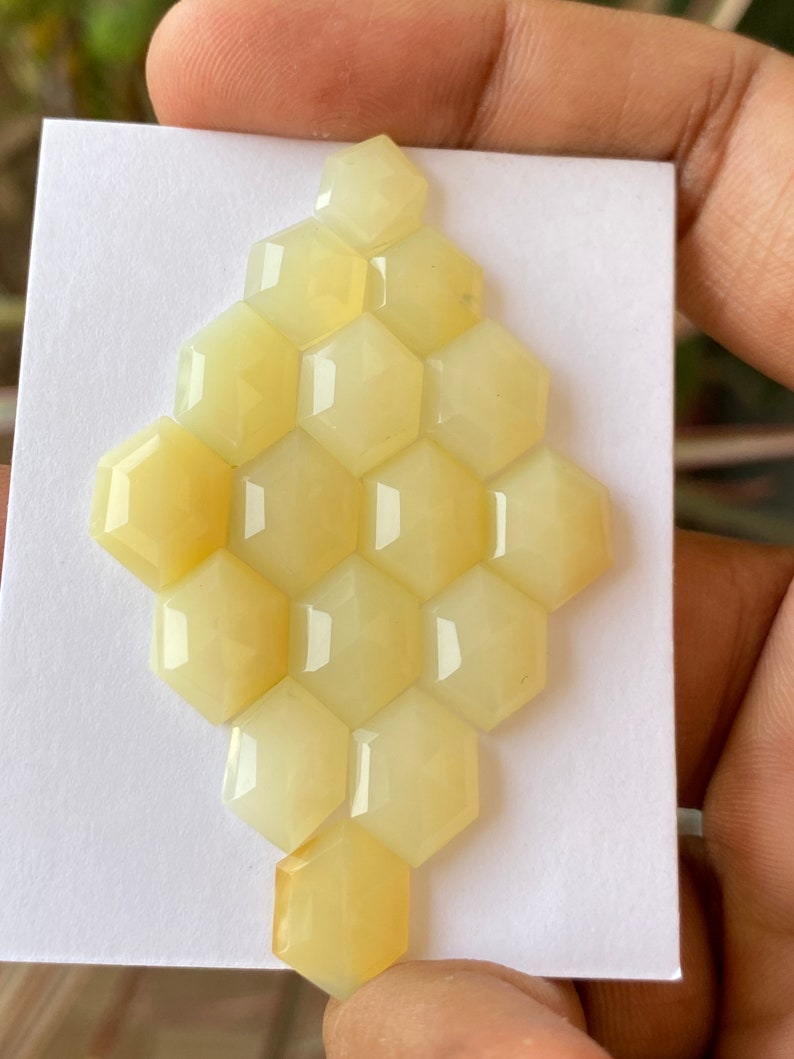 Peut inclure: Une collection de 15 pierres pr&eacute;cieuses hexagonales en cabochon jaune p&acirc;le dispos&eacute;es en nid d'abeille sur une carte blanche.
