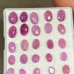 Puede incluir: Una colección de gemas rosas ovaladas y facetadas, dispuestas en una bandeja de plástico blanco. Las gemas varían en tonalidad, desde rosa claro a intenso, con inclusiones internas visibles. La bandeja es sostenida por una mano.