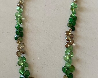 May include: A green and brown gemstone necklace with a graduated color pattern. The necklace is made of faceted oval-shaped stones.