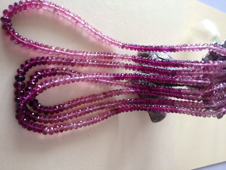 May include: Multiple strands of faceted gemstone beads in shades of pink and purple. The beads are strung together, creating a cascading effect. The colour gradient ranges from light pink to deep magenta.