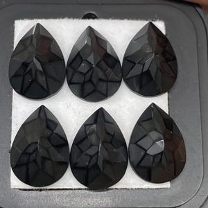 Può includere: Sei pietre preziose nere a forma di pera con superfici sfaccettate sono esposte in una scatola foderata in velluto nero.