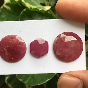 May include: Three pink gemstone cabochons, two round and one hexagonal, on a white card.