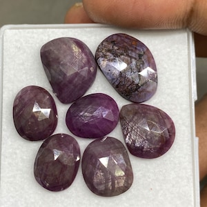 May include: Seven loose purple gemstones with a faceted cut. The gemstones are displayed in a white box.