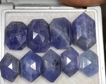 May include: A collection of eight faceted, blue gemstone beads in a small, white, velvet-lined box. The beads are arranged in two rows, with four beads in each row.