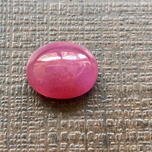 Puede incluir: Una piedra preciosa ovalada de color rosa con una superficie lisa y pulida.
