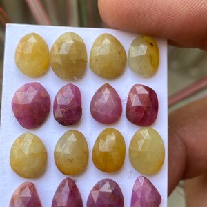 Peut inclure: Une collection de 18 cabochons de pierres précieuses facettées, 9 jaunes et 9 roses, disposés en rangées sur une carte blanche. Les pierres précieuses sont toutes de forme poire et ont une taille facetée.