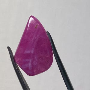 以下が含まれることがあります： ピンセットで保持された、涙の形をした白い筋のあるピンクの宝石