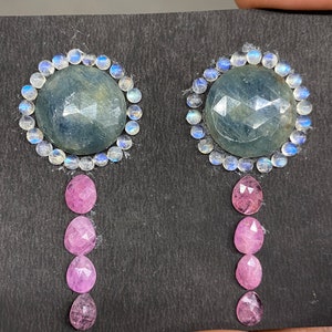 Puede incluir: Un par de pendientes con una piedra preciosa azul rodeada de piedras preciosas blancas y una piedra preciosa rosa colgante.
