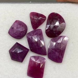 May include: Seven faceted purple gemstones of various shapes and sizes. The gemstones are displayed on a white surface.
