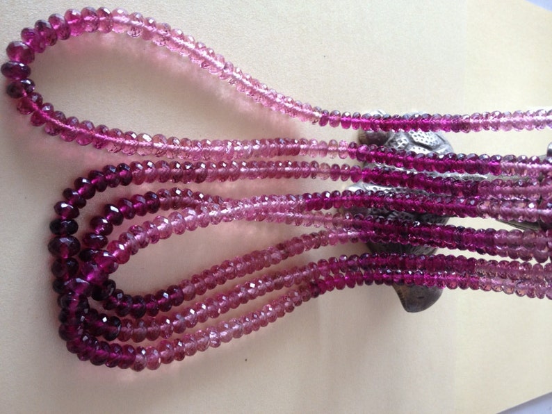 May include: Multiple strands of faceted gemstone beads in shades of pink and purple. The beads are strung to create necklaces, with a colour gradient from light pink to deep purple. The necklaces are draped, displaying the colour transition.