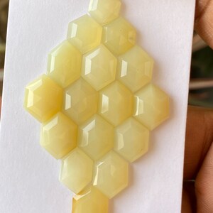 Peut inclure: Une collection de 16 pierres pr&eacute;cieuses hexagonales jaunes en cabochon dispos&eacute;es en nid d'abeille sur un fond blanc.