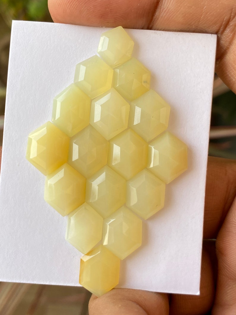 Peut inclure: Une collection de 16 pierres pr&eacute;cieuses hexagonales jaunes en cabochon dispos&eacute;es en nid d'abeille sur un fond blanc.