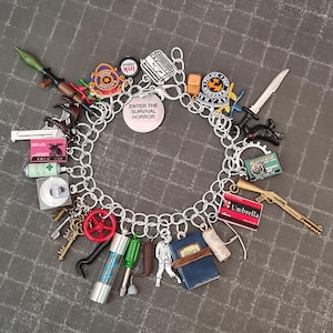 May include: A silver charm bracelet featuring a variety of charms, including a red and blue "Umbrella" charm, a green and black "Enter the Survival Horror" charm, a red and black "Police Station" charm, and a black and white "Diary" charm.