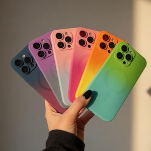 May include: A collection of six smartphone cases arranged in a fan shape, featuring a smooth gradient finish. The colors transition from deep blue to purple, light pink, vibrant pink, orange, and bright green, each with a circular magnetic ring.