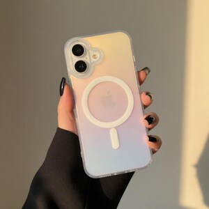 May include: A clear phone case with a pastel gradient of yellow, pink, and blue. The case features a white circular MagSafe charger and a white Apple logo. The phone case is held in a hand with black nail polish.