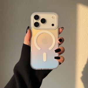 May include: A clear phone case with a gradient design of yellow, peach, and blue. The case has a white circular magnetic ring and a white vertical bar. The phone case has a camera cutout with three lenses.