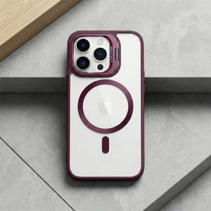 Może przedstawiać: Przezroczyste etui na iPhone'a z ciemnofioletową obwódką i pierścieniem aparatu. Etui posiada okrągły magnetyczny obszar ładowania i mały prostokątny magnetyczny punkt mocowania. Słowo "BRACKET" jest wydrukowane.