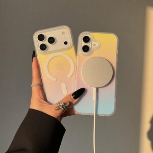 May include: Two clear phone cases with a gradient yellow, pink, and blue design. One case has a white magnetic charging circle attached. The cases are held up against a neutral background.