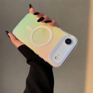 May include: Iridescent phone case with a white circular MagSafe charger. The case has a clear border and a camera cutout. The case reflects yellow, green, and pink hues. The phone case is designed to protect the phone.