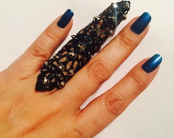 May include: A full-finger ring featuring a black, intricate, openwork lattice design that covers the entire length of the finger. The surface is embellished with numerous small, dark, faceted crystals that catch the light, creating a textured appearance.