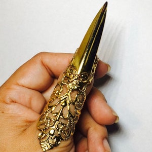 May include: A gold-colored, ornate, pointed ring for the thumb. The ring is made of metal and has a detailed design.