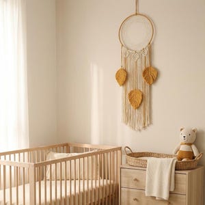 May include: A nursery scene featuring a light wood crib, a dresser with a woven basket, and a teddy bear. A large, circular dreamcatcher with mustard-colored leaf accents hangs on the wall, adding a bohemian touch to the room.